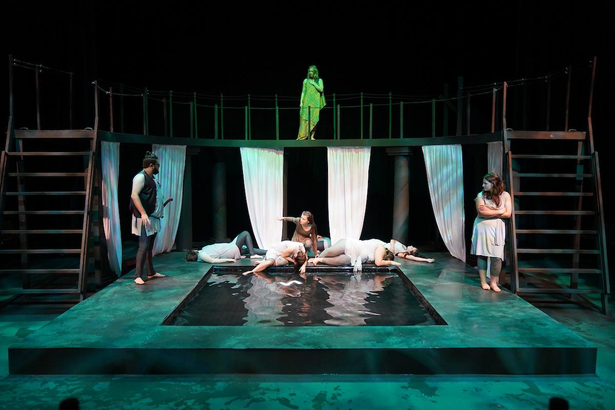 Students performing on stage with a courtyard like structure featuring a pool of water at the center