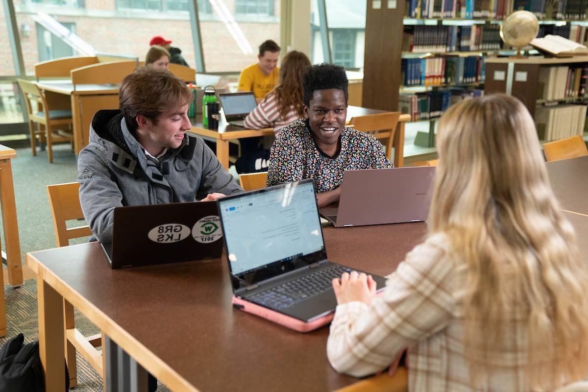 Students talking at a table with laptops open