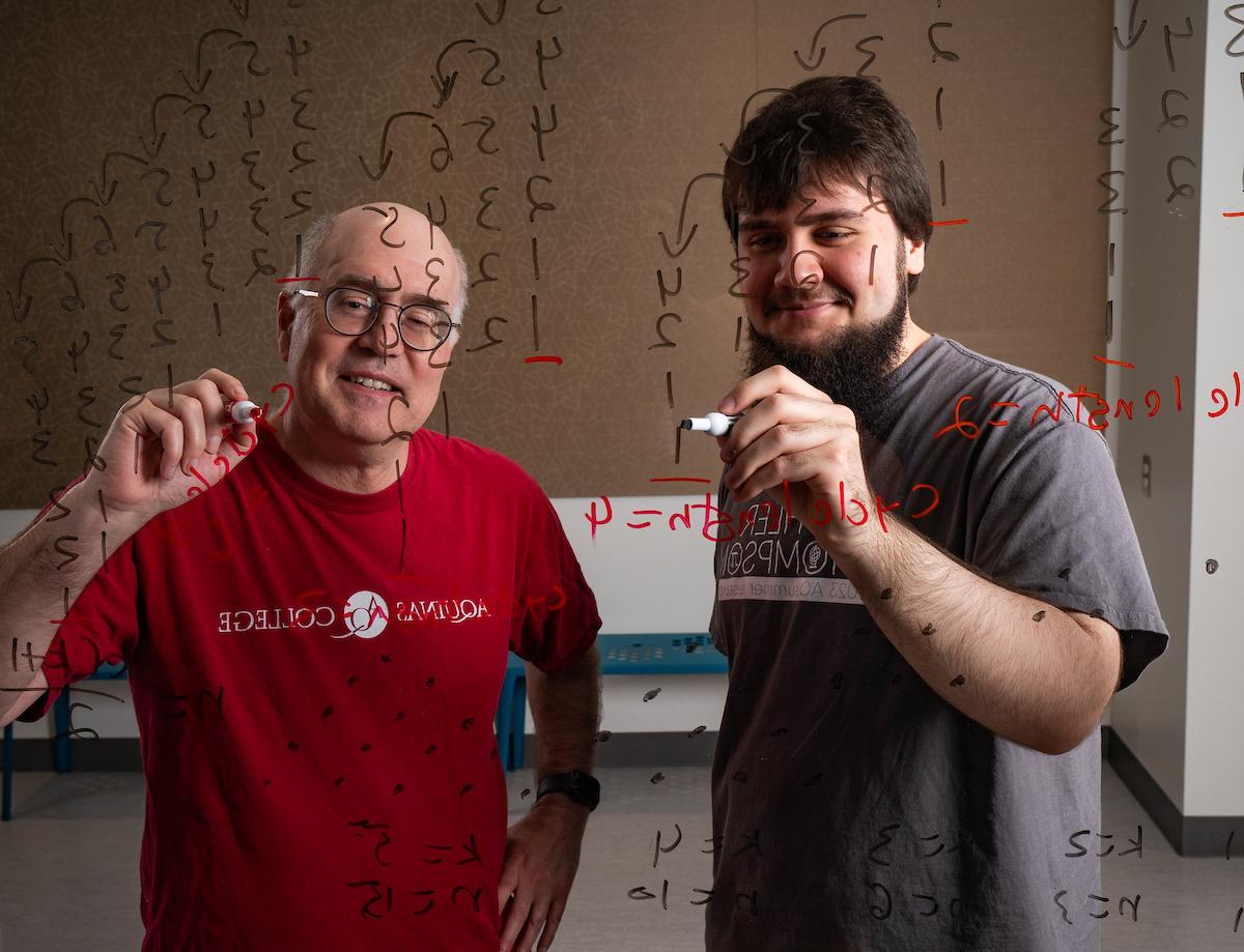 Mehanovic and Spencer holding dry erase markers up to a clear glass board full of numbers